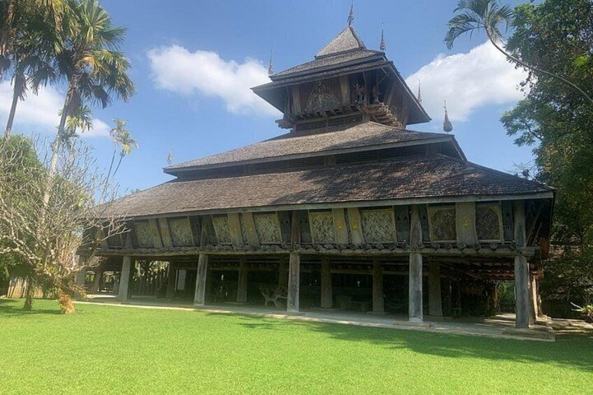 Ein traditioneller, mehrstöckiger Tempel mit Ziegeldach, umgeben von einem gepflegten Rasen und Palmen. 1
