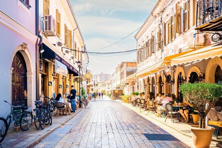 A cobblestone street lined with cafes and outdoor seating, bicycles parked along the side, and a clear sky. 1