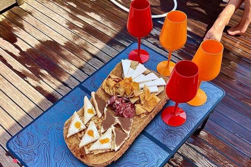 A wooden table with a blue patterned placemat, a loaf of bread with various toppings, and four red wine glasses. 2