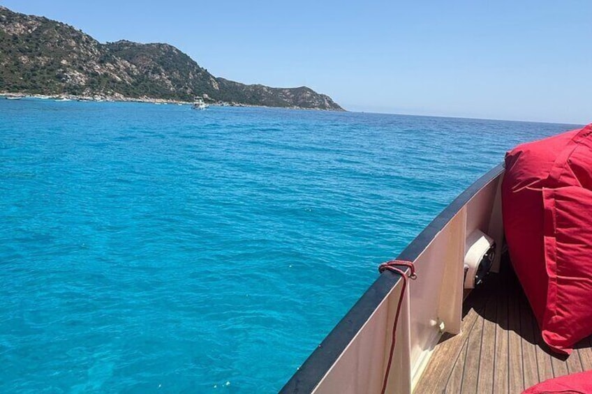 A boat on a clear blue sea with a rocky coastline in the background. 5