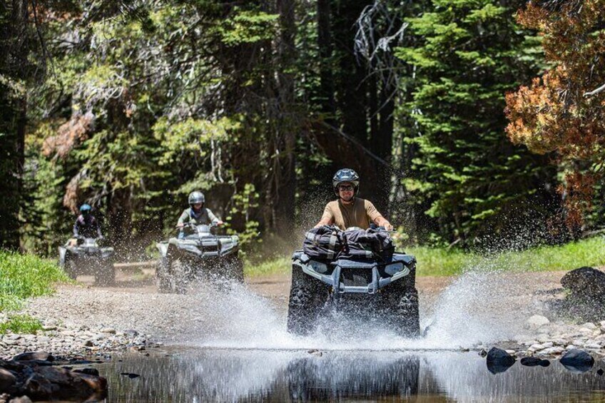 People riding ATVs on a dirt path near a water body. 1