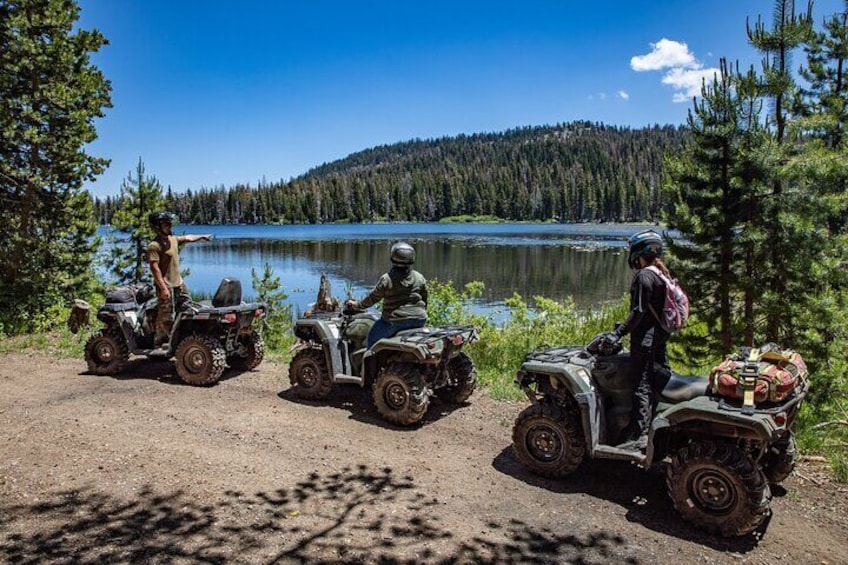 Three ATVs parked by a lake with a forest in the background. 5