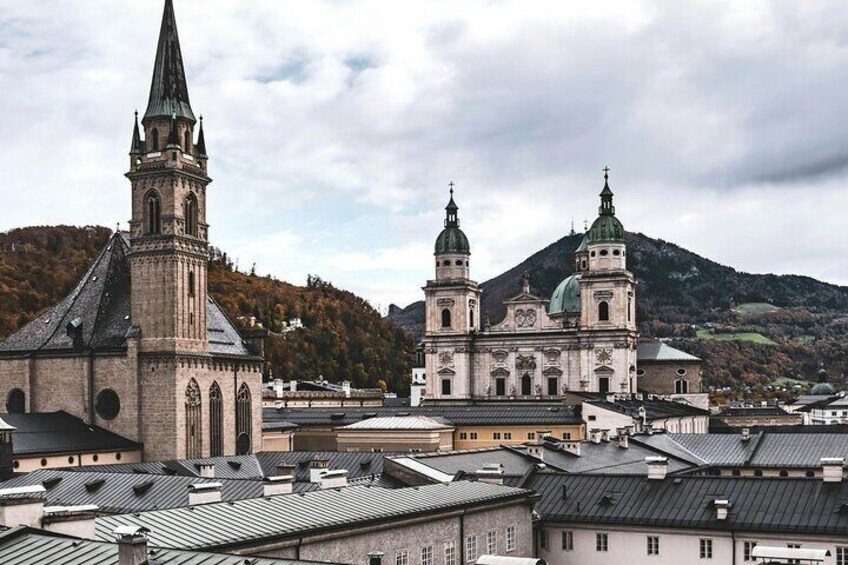 A historic church with a tall spire and a large dome, surrounded by buildings and a mountainous backdrop. 3