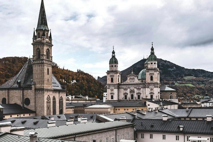 A historic church with a tall spire and a large dome, surrounded by buildings and a mountain in the background. 2