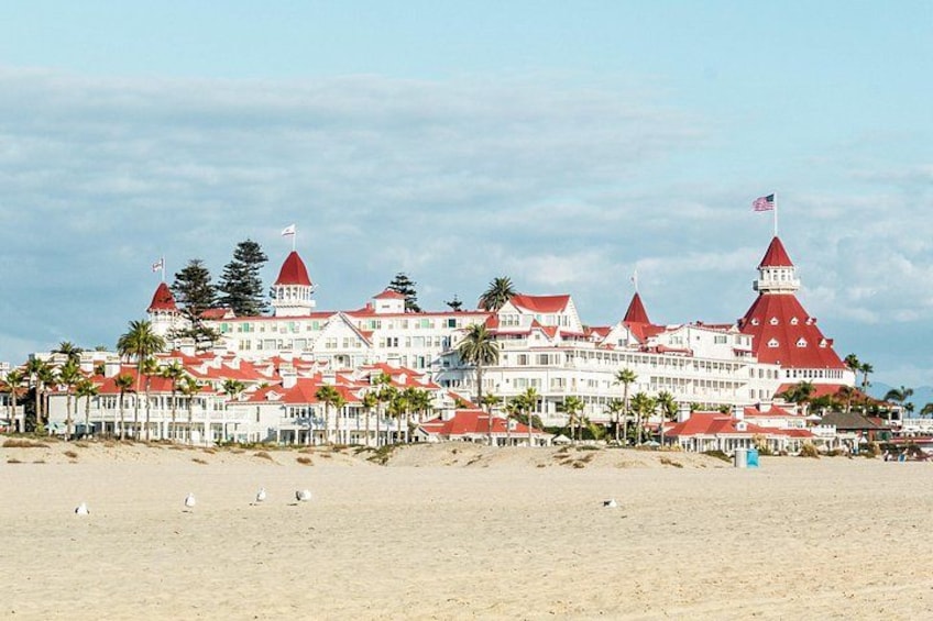 A large hotel with red roofs and multiple towers, situated on a beach with palm trees. 3