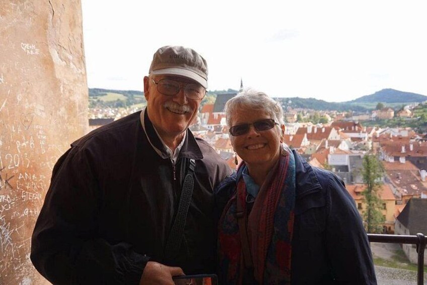 Two people standing on a balcony with a view of a town and hills in the background. 4