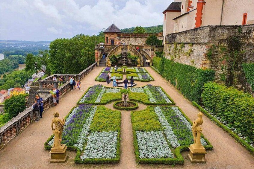 A garden with statues, a castle, and a river in the background. 2