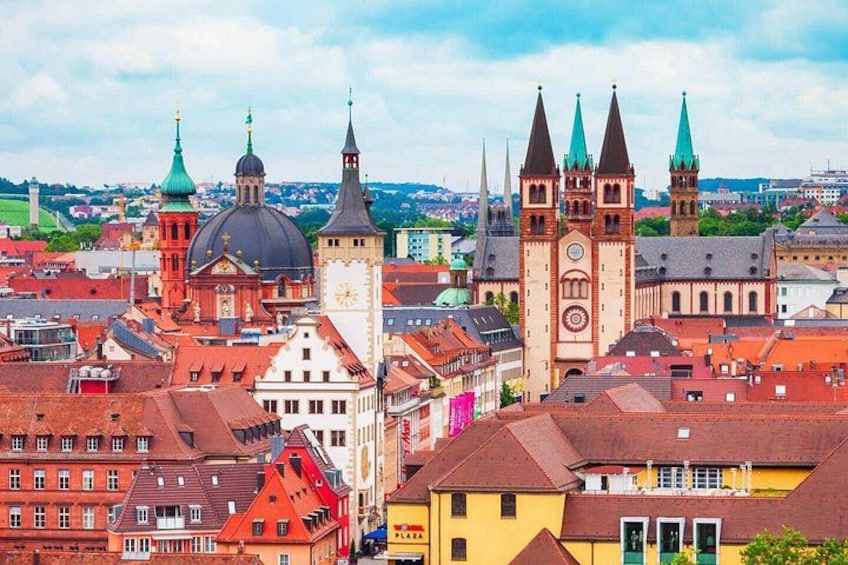 A cityscape with historic buildings, a prominent clock tower, and a church with multiple spires. 1