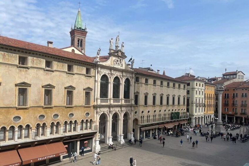 A historic square with a prominent building featuring arched windows and a bell tower. 4