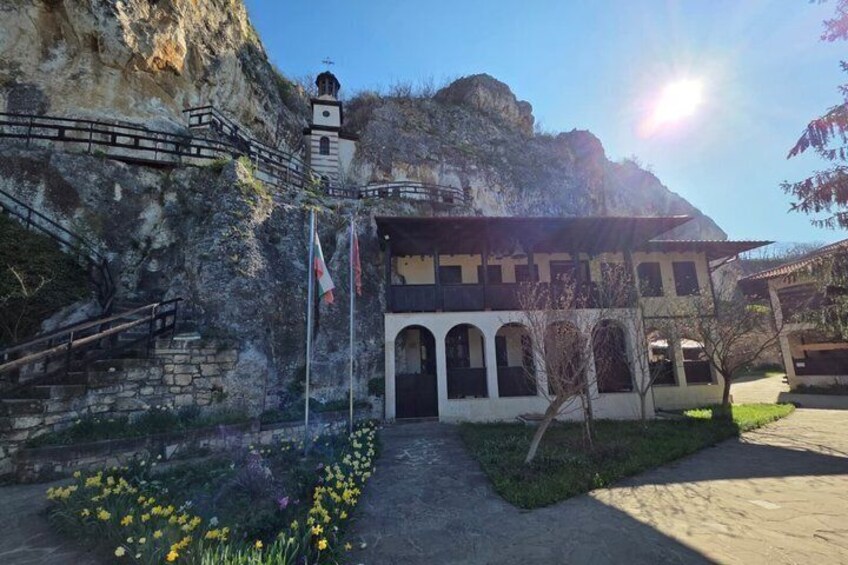 A building with a bell tower, surrounded by a stone wall and a pathway with flowers. 2