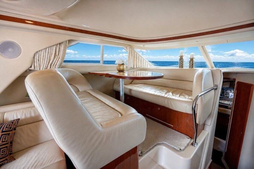A boat interior with a dining area, cushioned seating, and a view of the sea. 5
