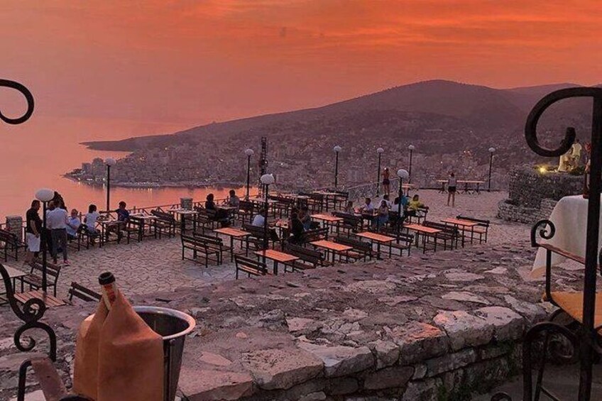 A seaside café with tables and chairs, overlooking a city and hills. 2