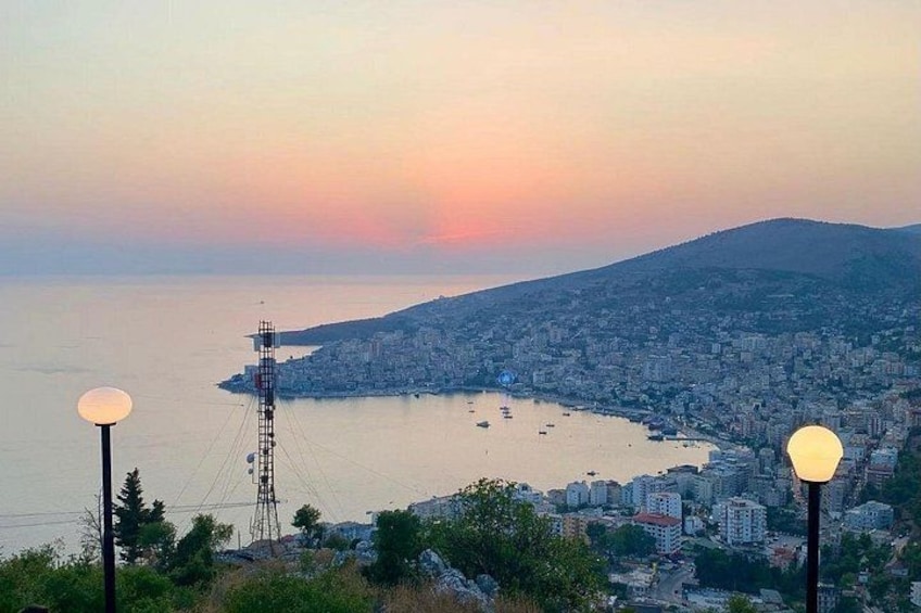 A coastal cityscape at sunset with a clear view of the sea, buildings, and a communication tower. 3