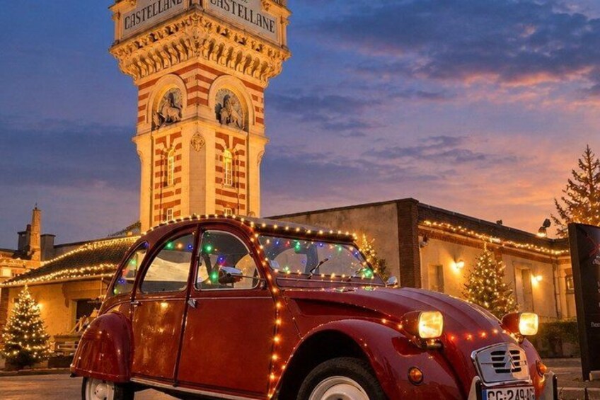 A vintage car with lights, a clock tower, and Christmas trees. 1
