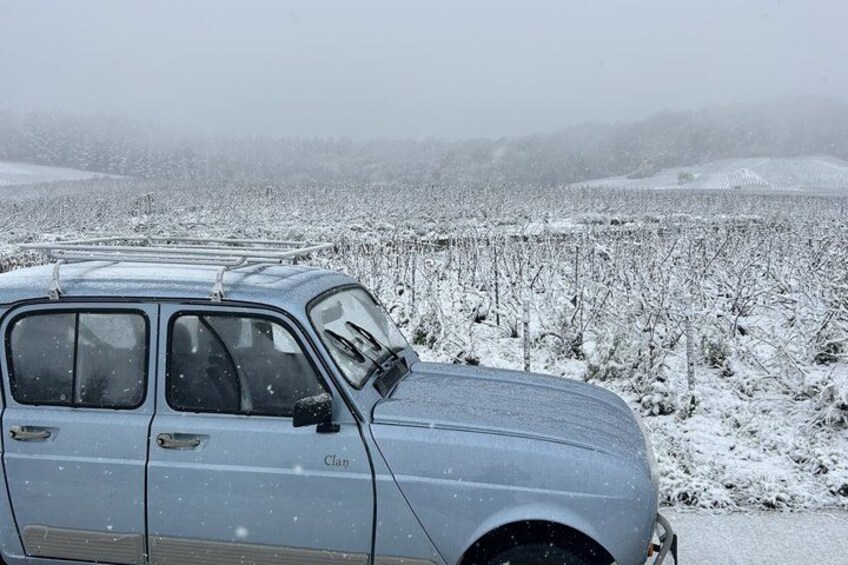 A vintage car parked in a snowy field with a distant mountain range. 2