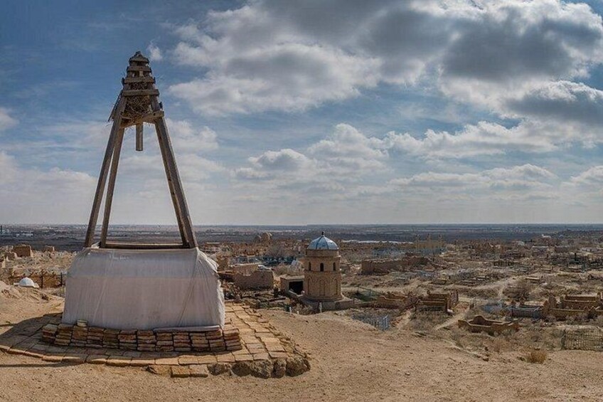 A desert landscape with a large, white, pyramid-like structure in the foreground and a distant view of a cityscape under a cloudy sky. 2