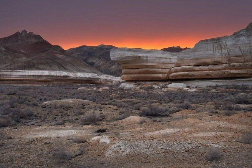 A desert landscape with layered rock formations and a sunset. 3