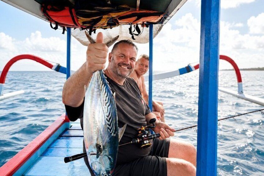 A person giving a thumbs-up gesture, holding a fish, and sitting on a boat with a blue and red structure. 2