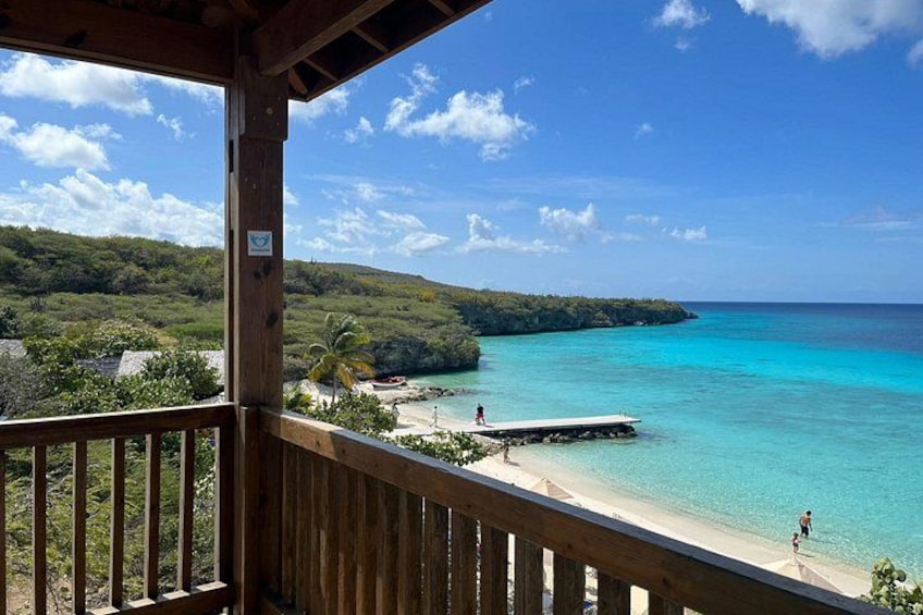 A wooden deck overlooking turquoise waters, a beach, and a lush green landscape. 2