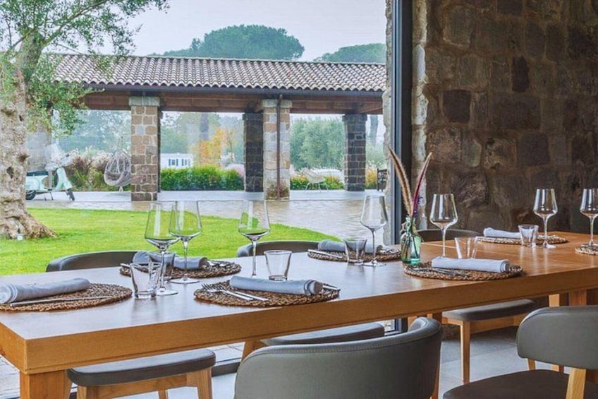 A dining table set for a meal with chairs, a stone wall, and a view of a garden and building in the background. 2