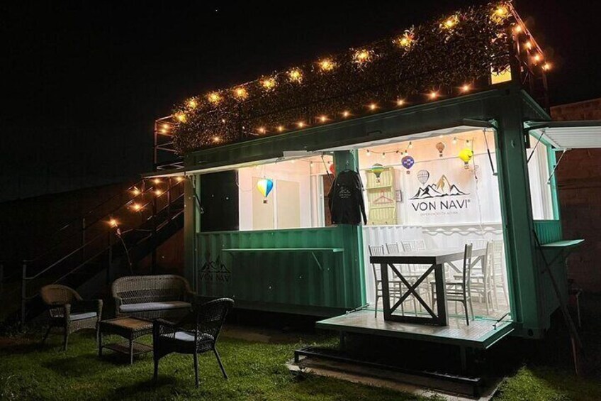 A green outdoor seating area with chairs and a table, illuminated by string lights. 2