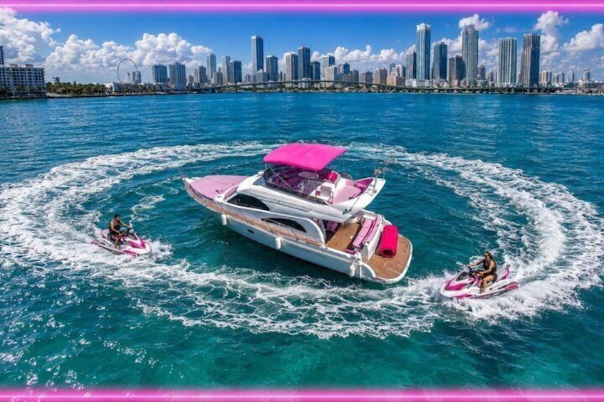 A yacht with a pink canopy, two jet skis, and a city skyline in the background. 1