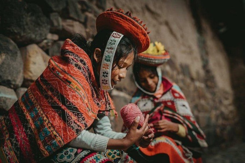 Two individuals in traditional attire sitting on a stone surface, one holding a pink object. 4