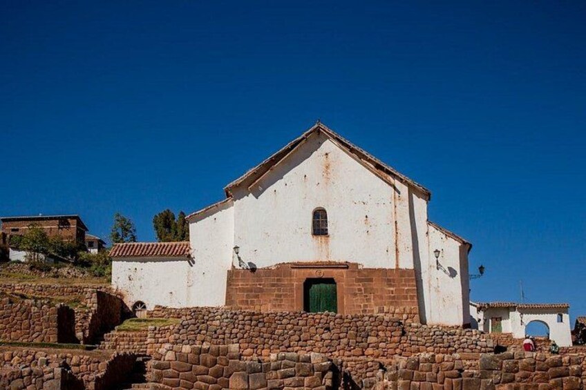 A white building with a green door, surrounded by stone walls and a clear blue sky. 4