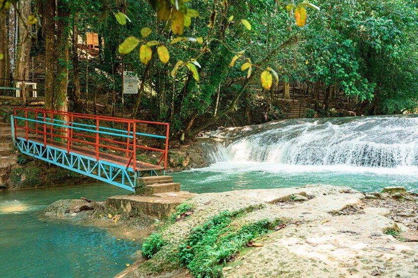 A red and blue bridge over a waterfall, surrounded by lush greenery. 3