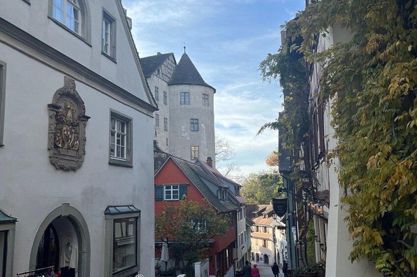 A narrow street with historic buildings, a tower, and ivy-covered walls. 2