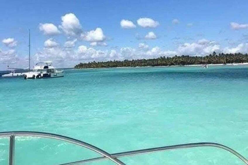 A clear turquoise sea, a boat, and a distant island with palm trees. 5