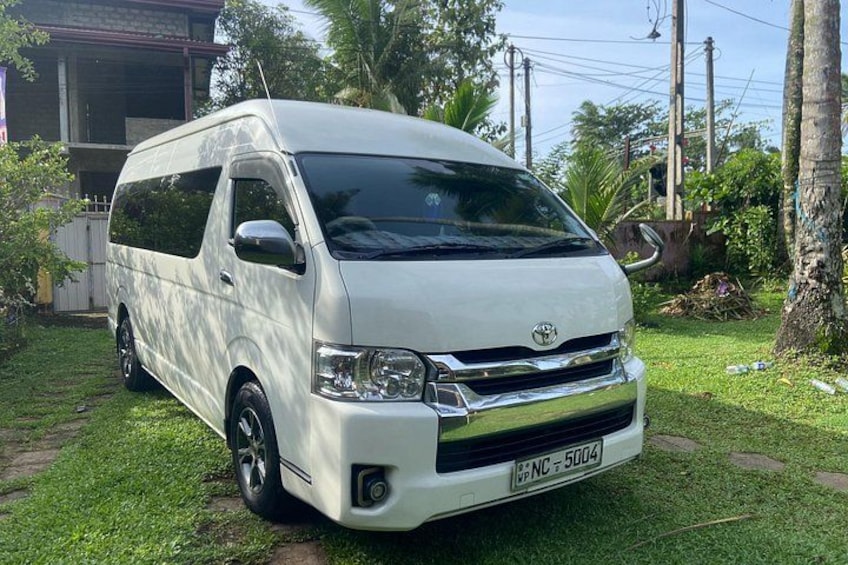 A white van parked on a grassy area with a house and trees in the background. 1