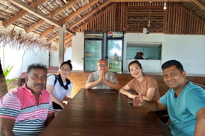 A group of people seated at a wooden table in a restaurant with a thatched roof and a Pepsi refrigerator in the background. 3