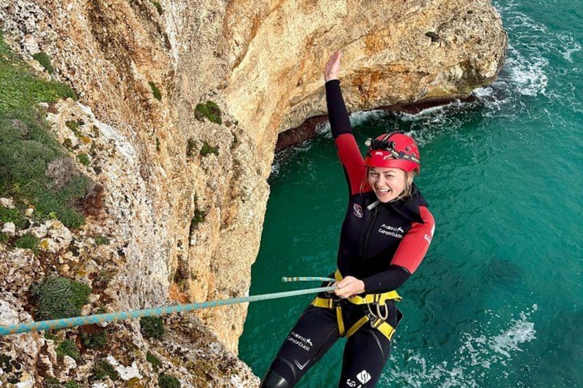 A person rappelling down a cliff with a rope, wearing a red helmet and black and red wetsuit. 2