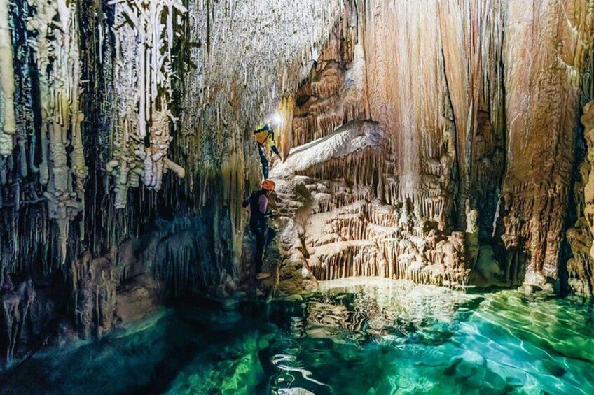 A cave with stalactites and stalagmites, a person exploring, and a water pool. 2