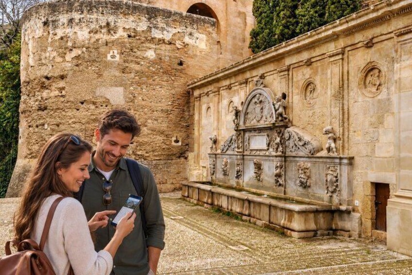 A couple standing in front of a historical building with detailed carvings and a stone wall. 2