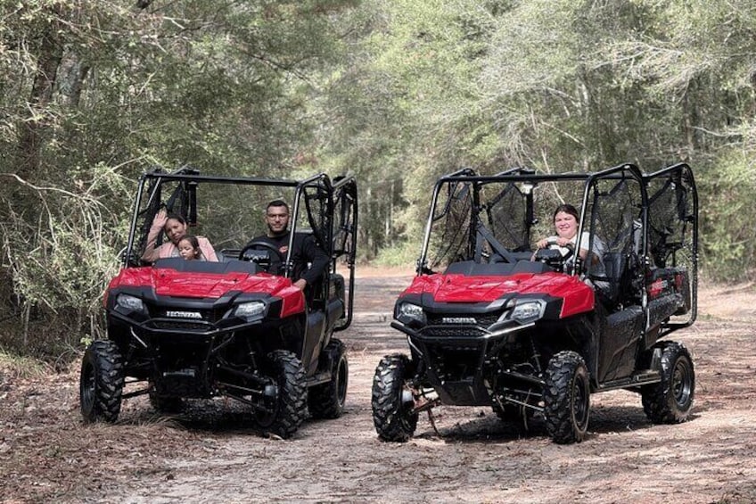 Two red Honda ATVs on a dirt road surrounded by trees. 3