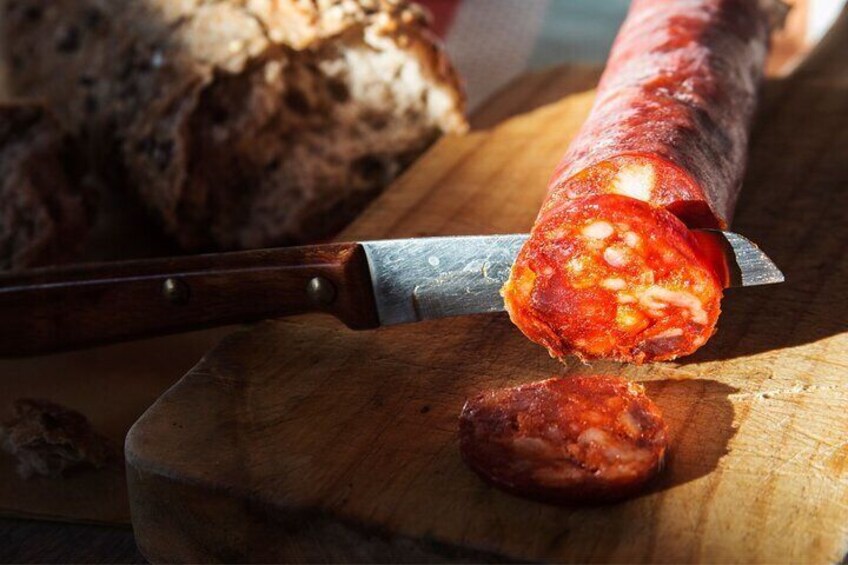 A sausage being sliced on a wooden cutting board. 3