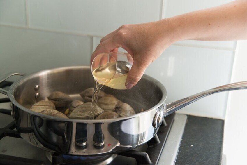 A hand pouring oil into a pan with clams on a stove. 2