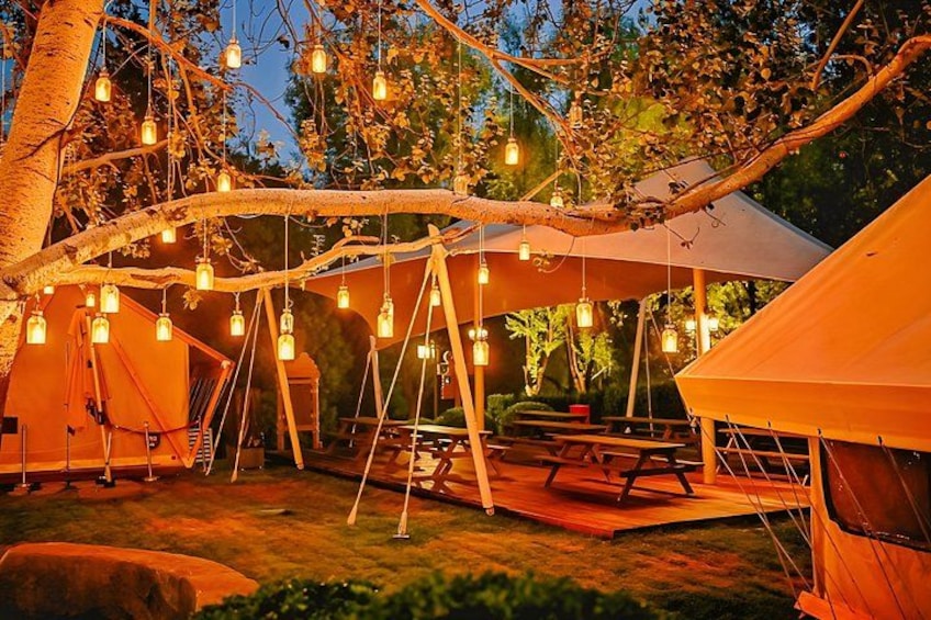 A campsite with tents, picnic tables, and string lights. 2