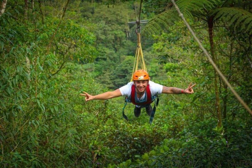 En person som hoppar bungyjump med sele och hjälm, omgiven av tät, grön vegetation. 2