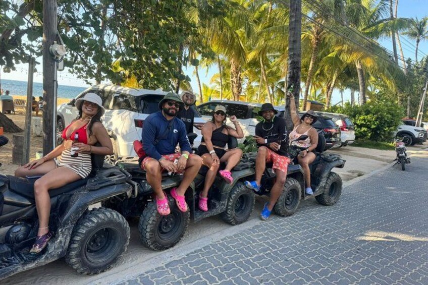 Eine Gruppe von Personen mit Geländefahrzeugen auf einer asphaltierten Straße, im Hintergrund Palmen und ein Strand. 4