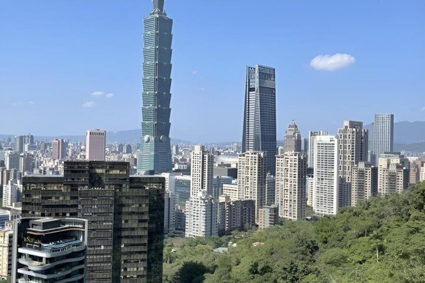 A cityscape with a prominent skyscraper, dense urban buildings, and a green hill in the foreground. 5