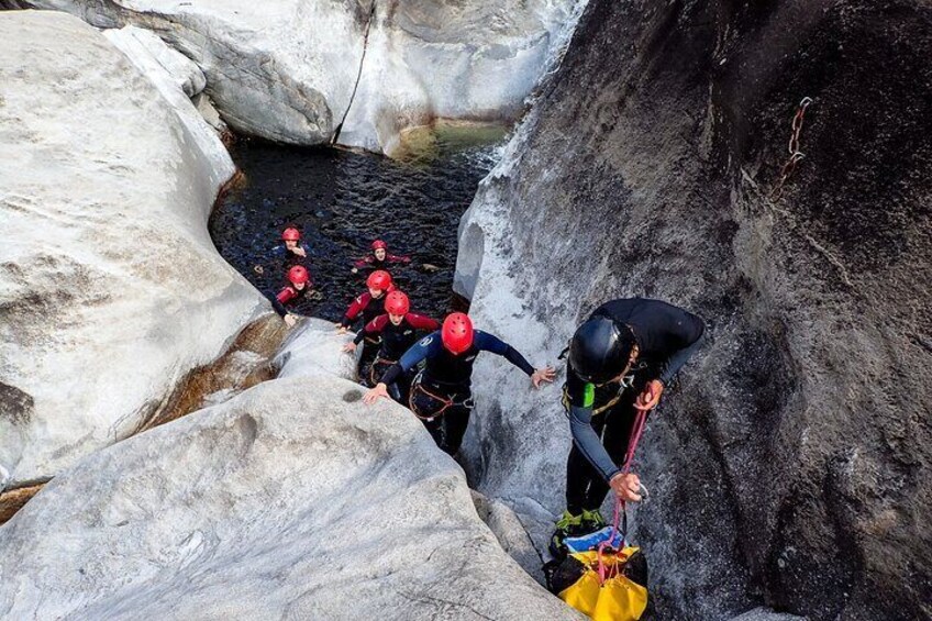 A group of people rappelling down a rocky cliff into a water-filled crevice. 2