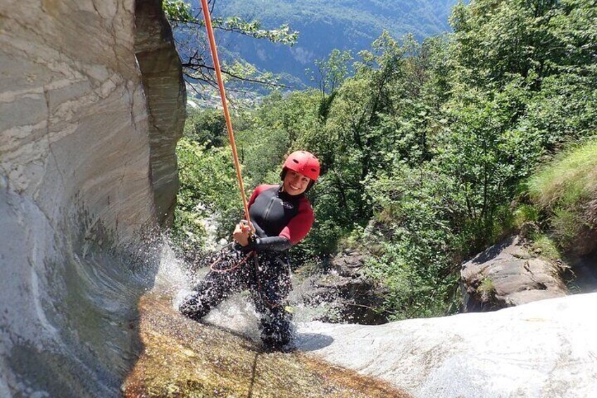 A person rappelling down a rocky cliff with a rope, surrounded by lush greenery and a mountainous landscape. 5