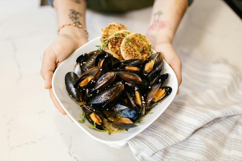 A person holding a bowl of mussels with a side of bread. 3