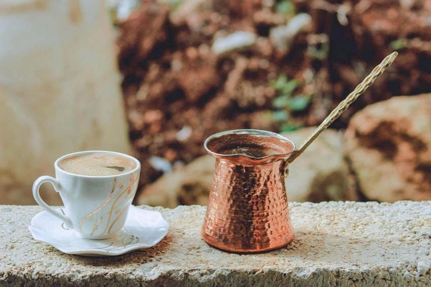 A white cup with a saucer and a copper pot with a spoon on a stone ledge. 2