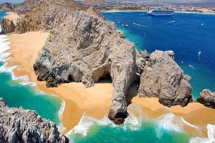 A coastal landscape with a prominent rock formation, a sandy beach, and clear blue waters. 2