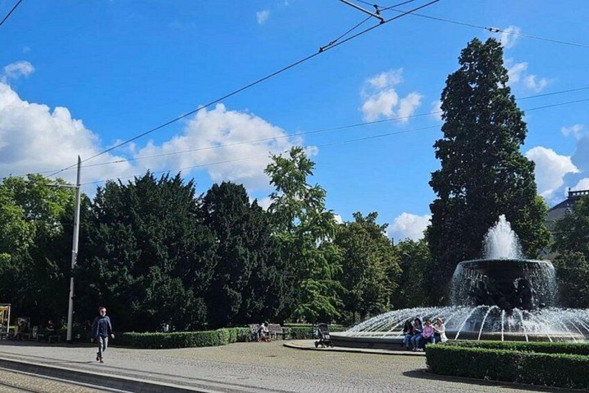 A park with a fountain, trees, and a clear blue sky. 3