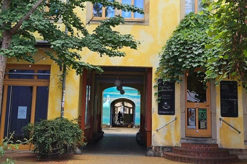 A building entrance with a yellow facade, a wooden door, and a staircase leading to a covered area. 2